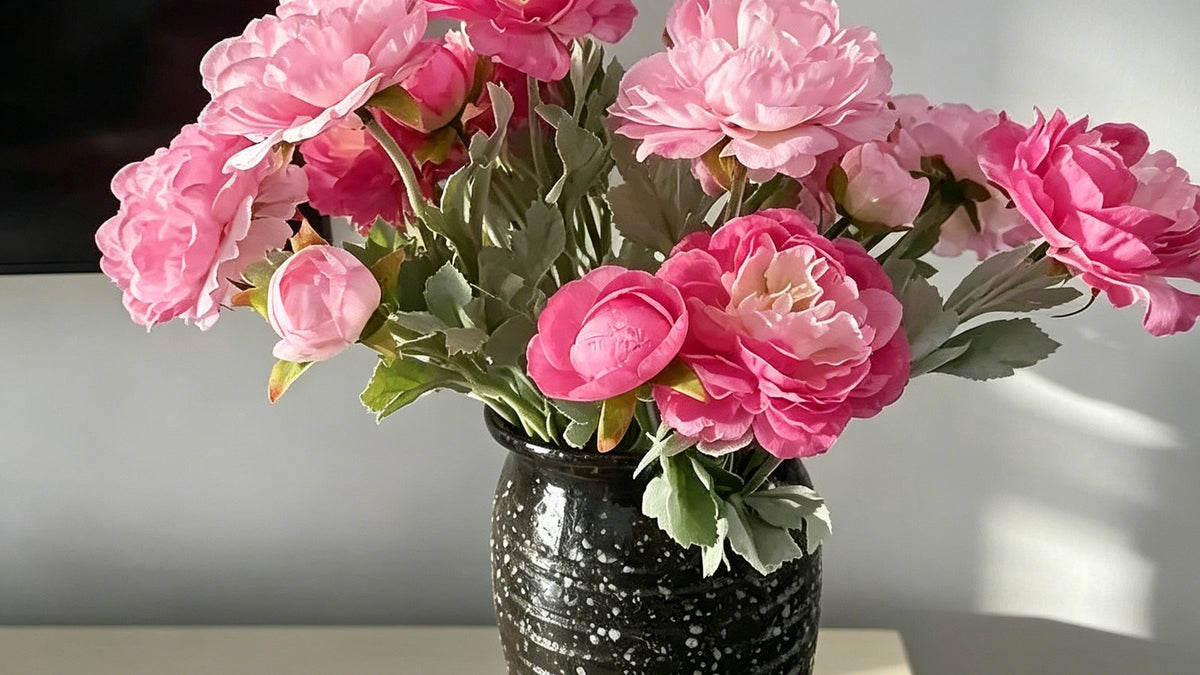 Pink artificial peony blooms and buds arranged in a black vase